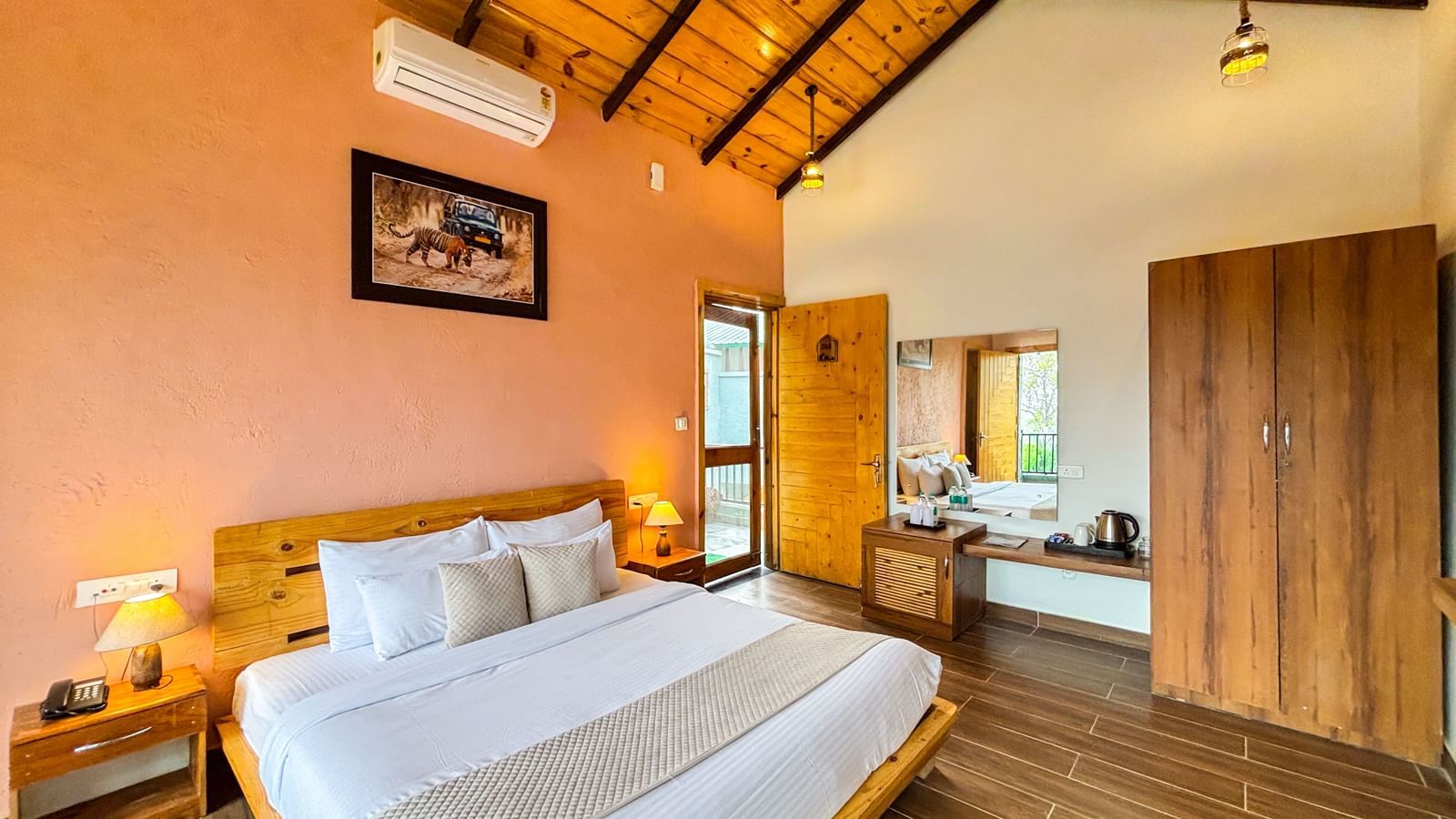 A cosy bedroom with a sloped wooden ceiling, a large bed, and warm-toned walls at Corbett Nirvana Resort..