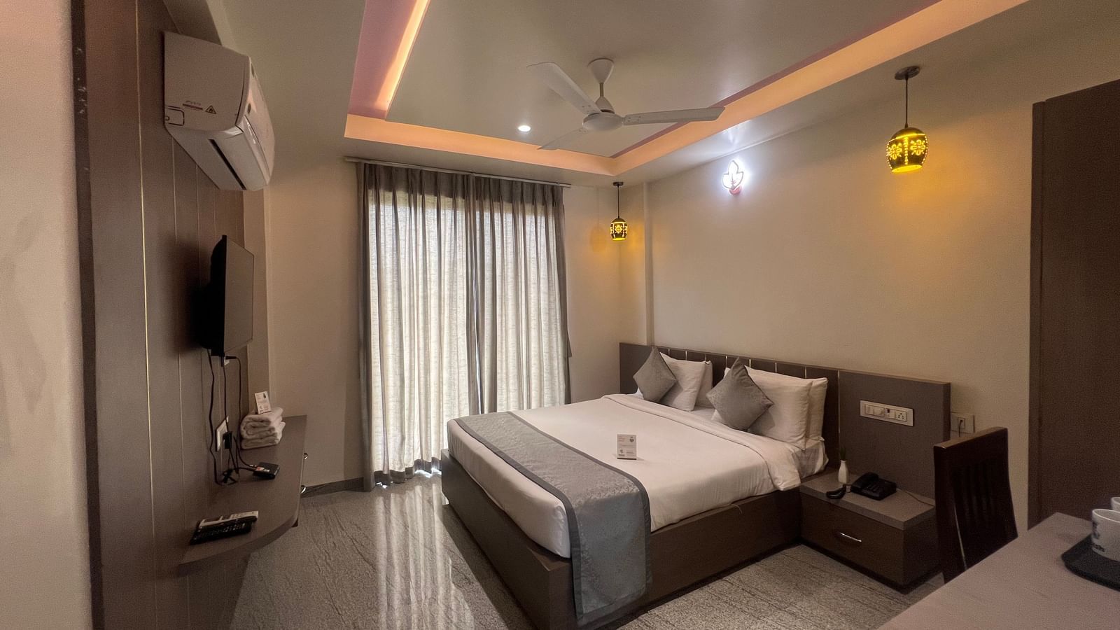 Wide view of the Daksh Bliss room at Daksh The Valley Resort, Saputara, featuring its queen size bed, closed curtains, and designer ceiling.