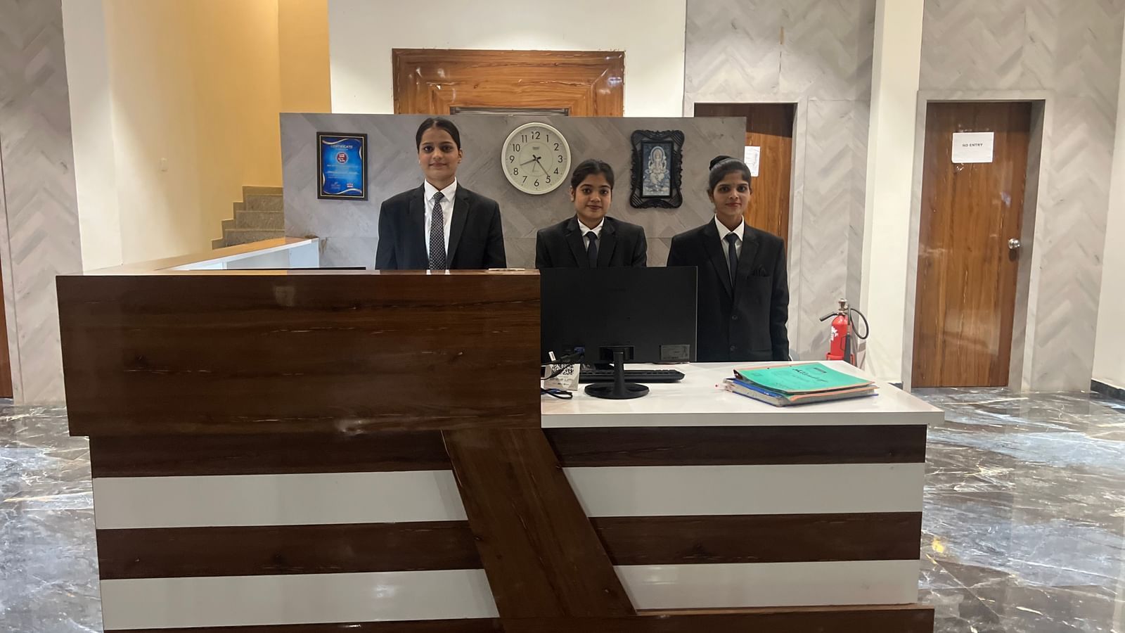3 people standing at the reception desk of Daksh The Valley Saputara, situated in the lobby area with marble flooring.