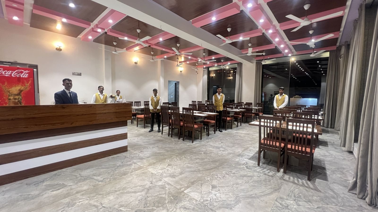 Wide view of the fine-dining restaurant at Daksh The Valley Resort, Saputara, showcasing its vibrant ceiling, neatly arranged dining tables and the staff standing there.