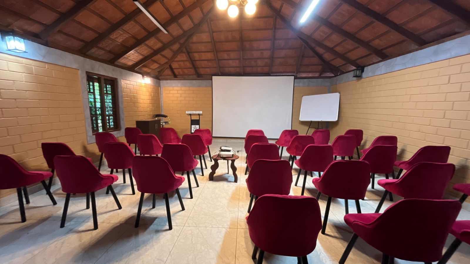 Interior of Robusta Meeting Hall at Evergreen County, Coorg featuring vaulted ceiling, brick walls and plush burgundy seating