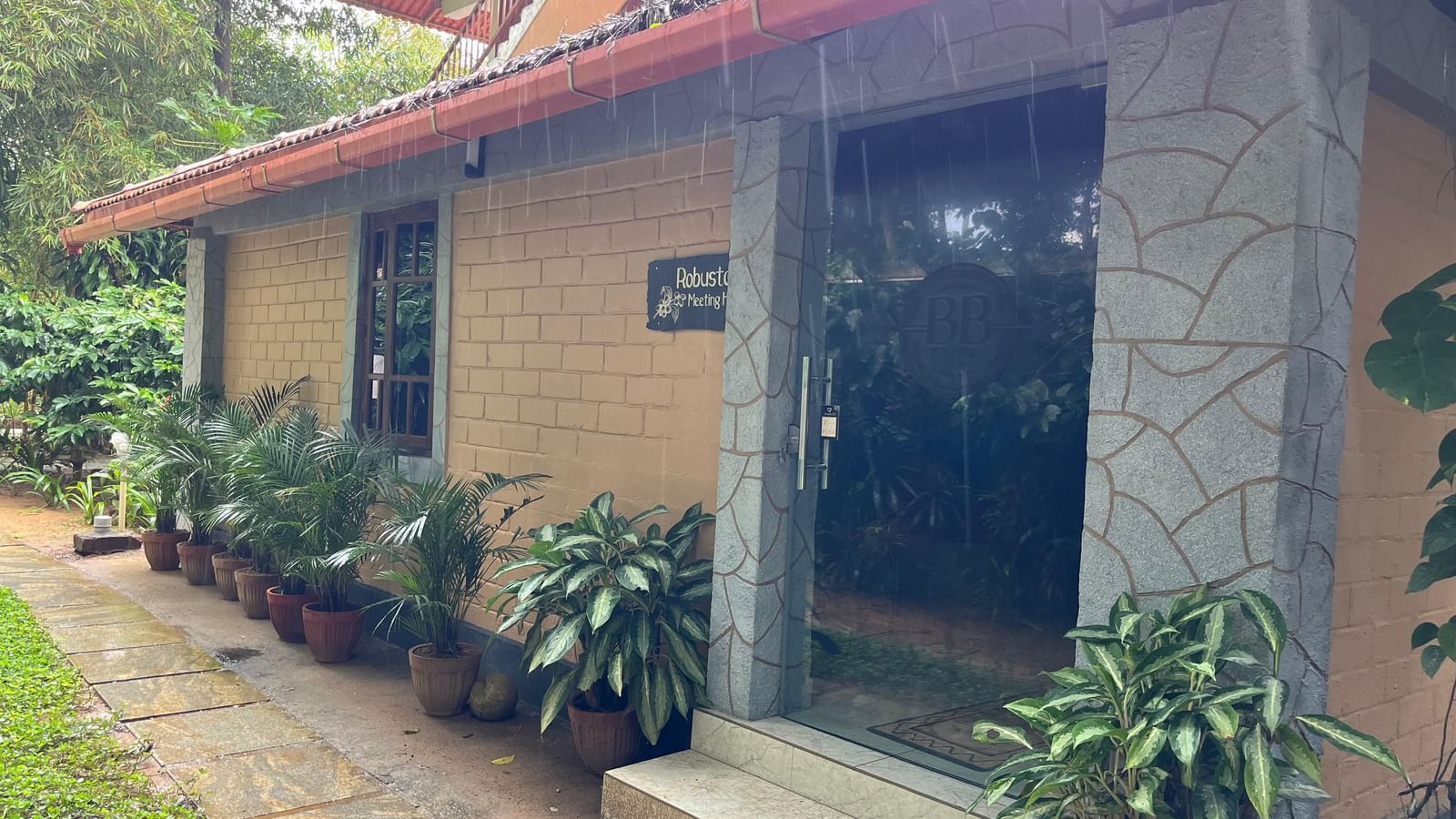 Exterior view of Robusta Meeting Hall at Evergreen County, Coorg surrounded by lush tropical plants and rustic architecture