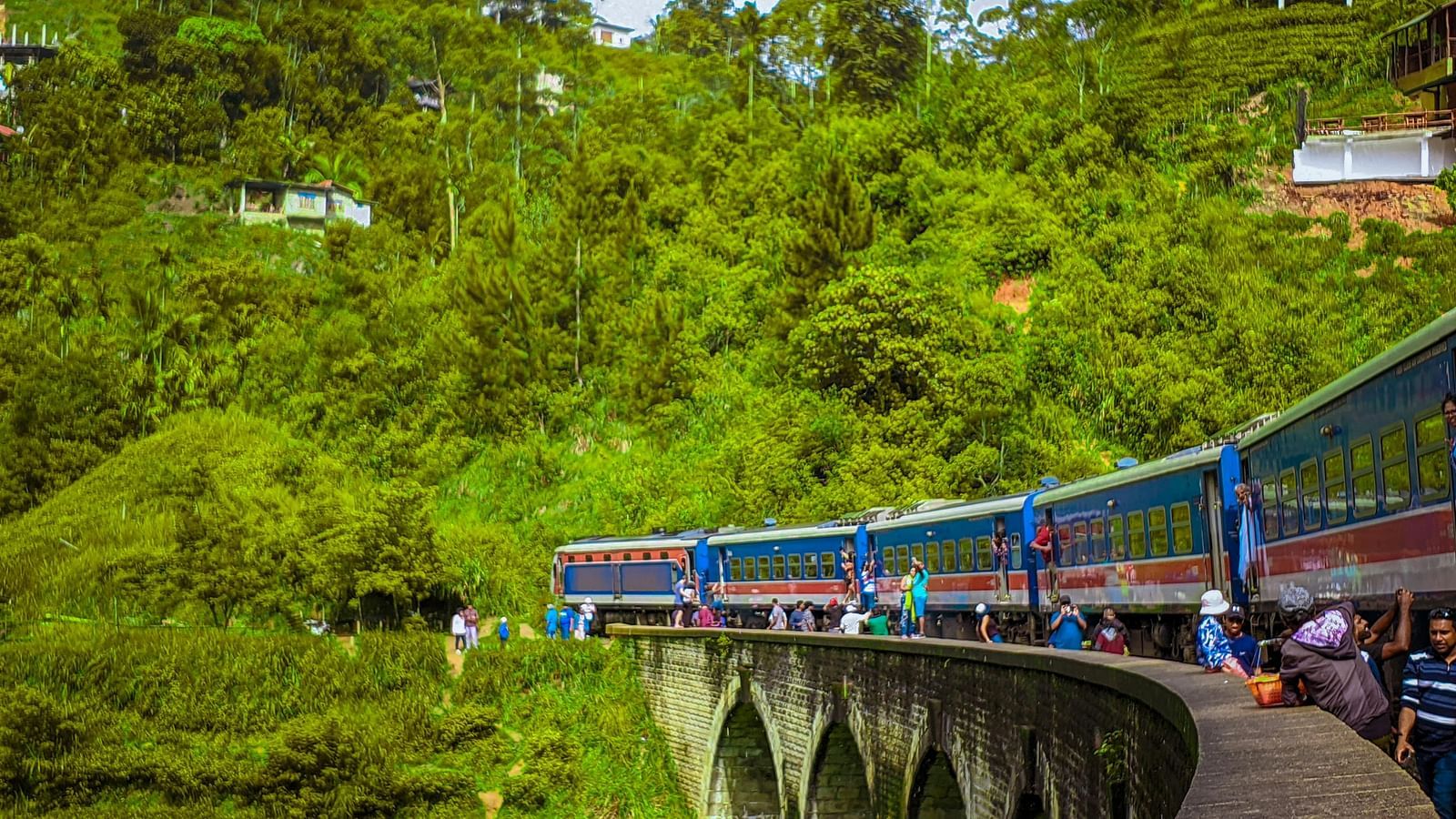 Train crossing a scenic stone bridge surrounded by lush greenery.