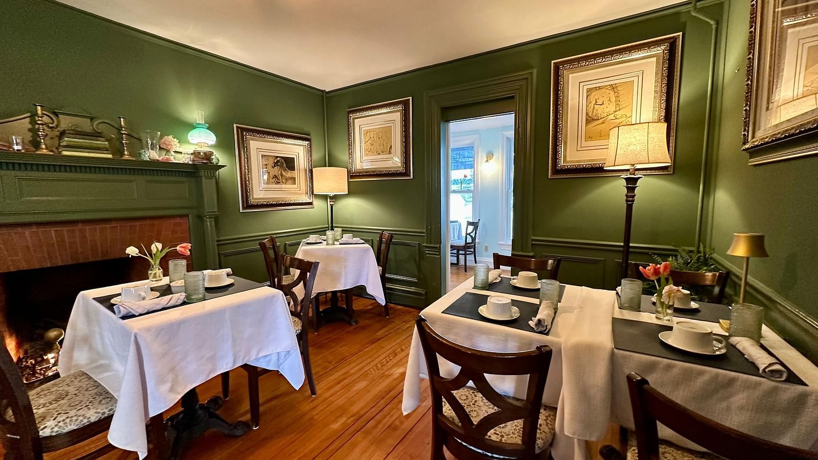 A dining room at Hartstone Inn featuring green walls, white tablecloths, and framed artwork