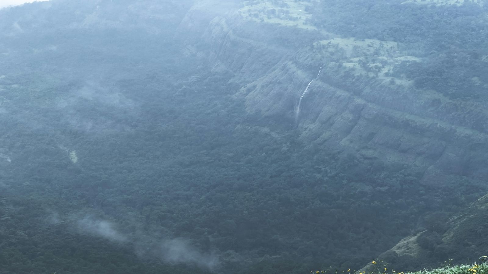 image of lush green mountains with a small stream of water falling from a height.