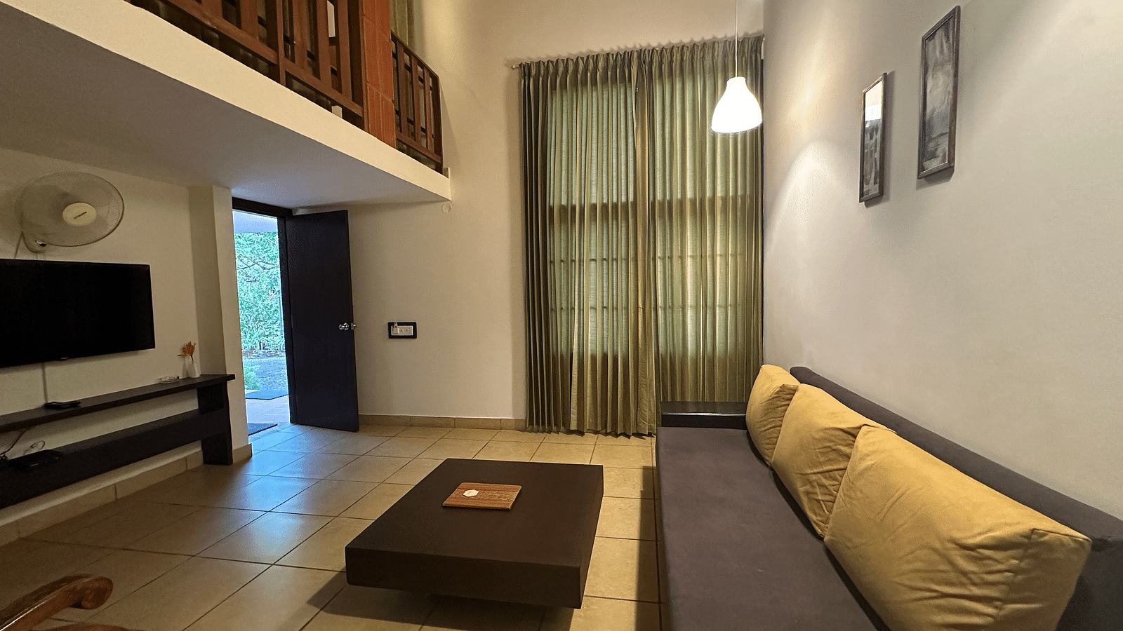 a living room with a long sofa and a television on the wall - Kadkani River Resort, Coorg