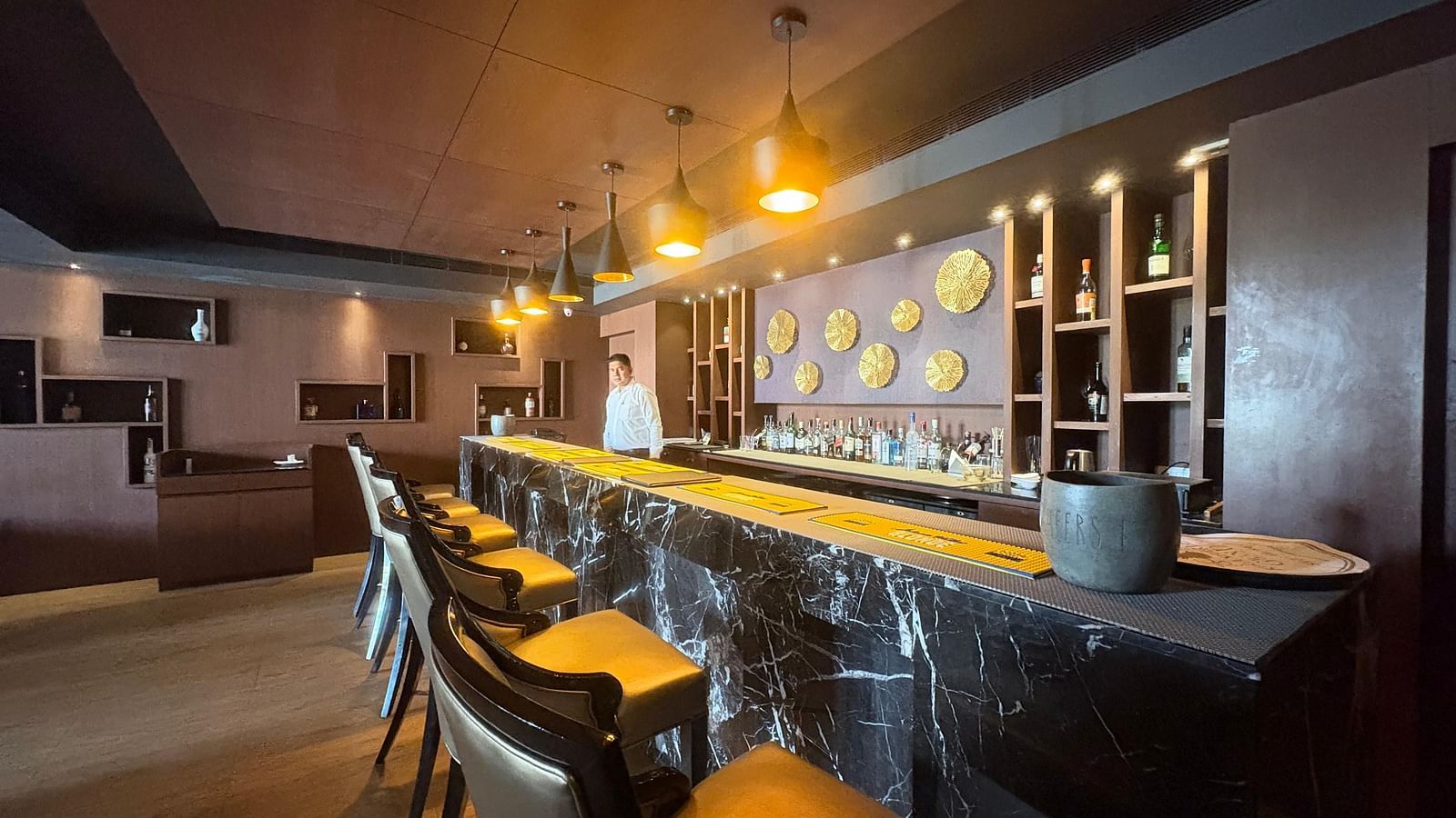 A bar with a dark, textured counter and yellow-toned bar stools, focusing on the bar's design elements and lighting.