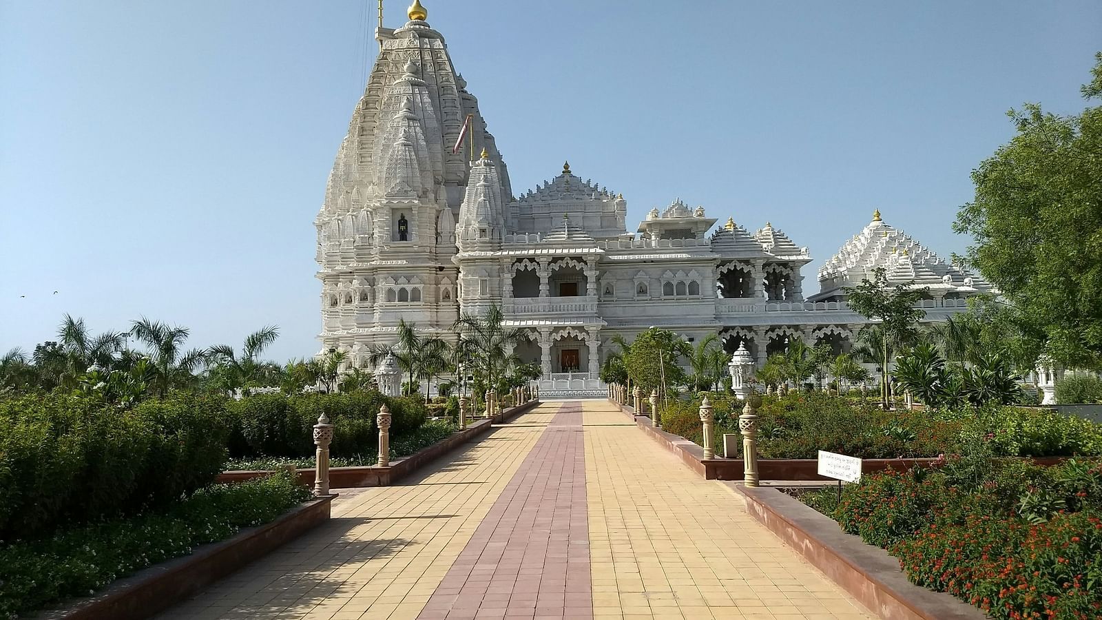 a white marbled temple in the distance with a pathway leading to it and shrubs on either side