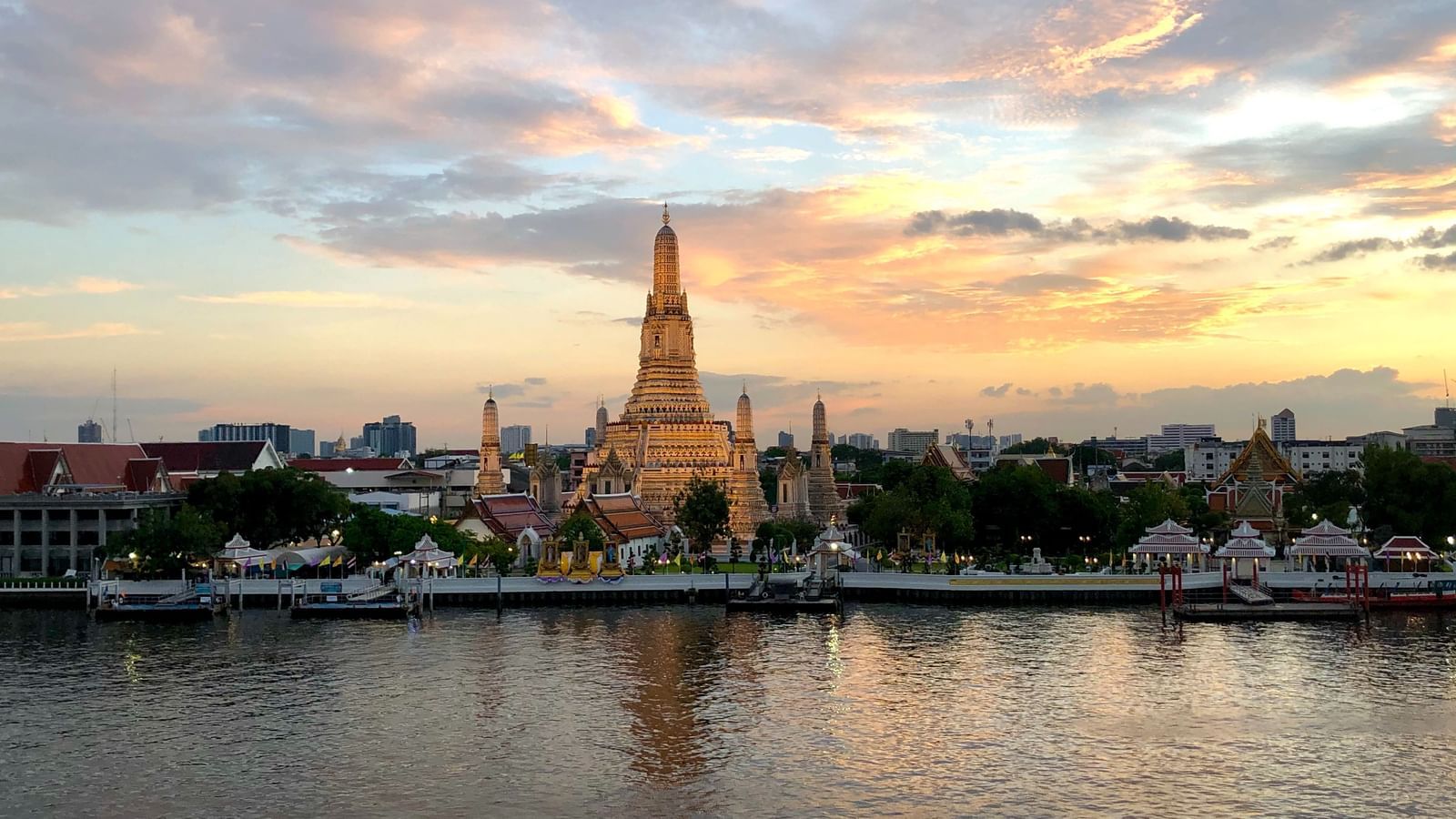 Wat Arun temple situated in front of the river front with buildings text to it - one of the must-visit Bangkok Tourist Places.