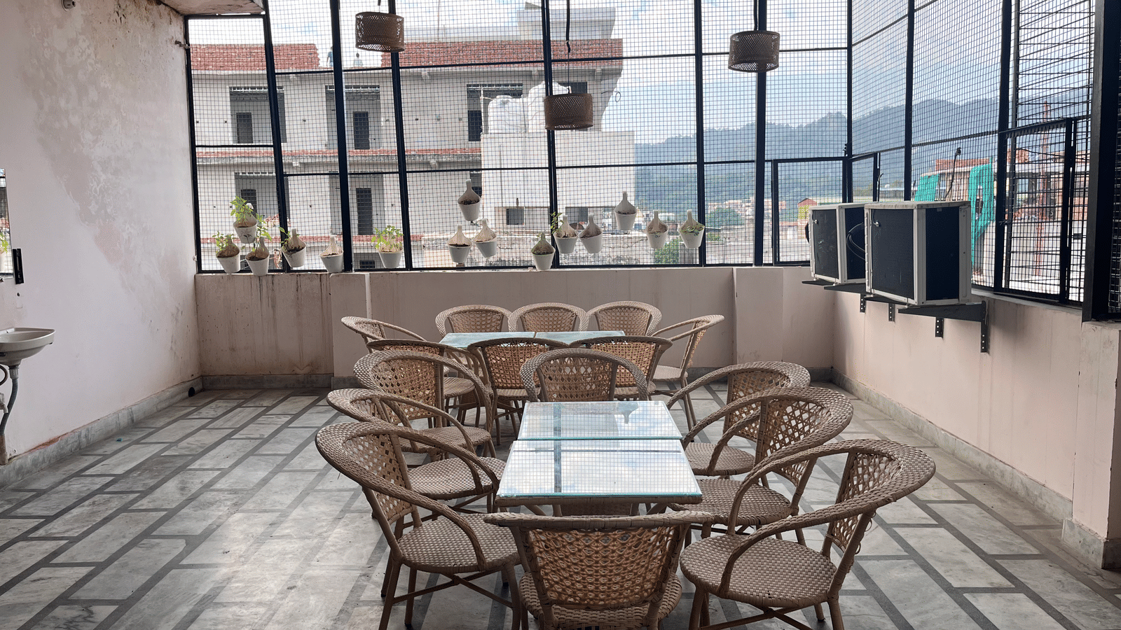 2 dining tables featuring a glass surface lined with bamboo chairs on the rooftop dining area at Perfectstayz Value Dhruv Nanda, Haridwar.