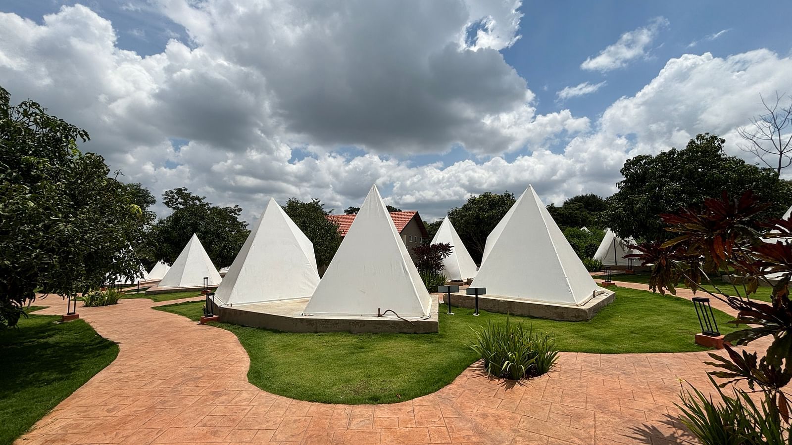 A scenic view of a resort area with tents lined along a neat walkway, surrounded by a well-maintained lawn.
