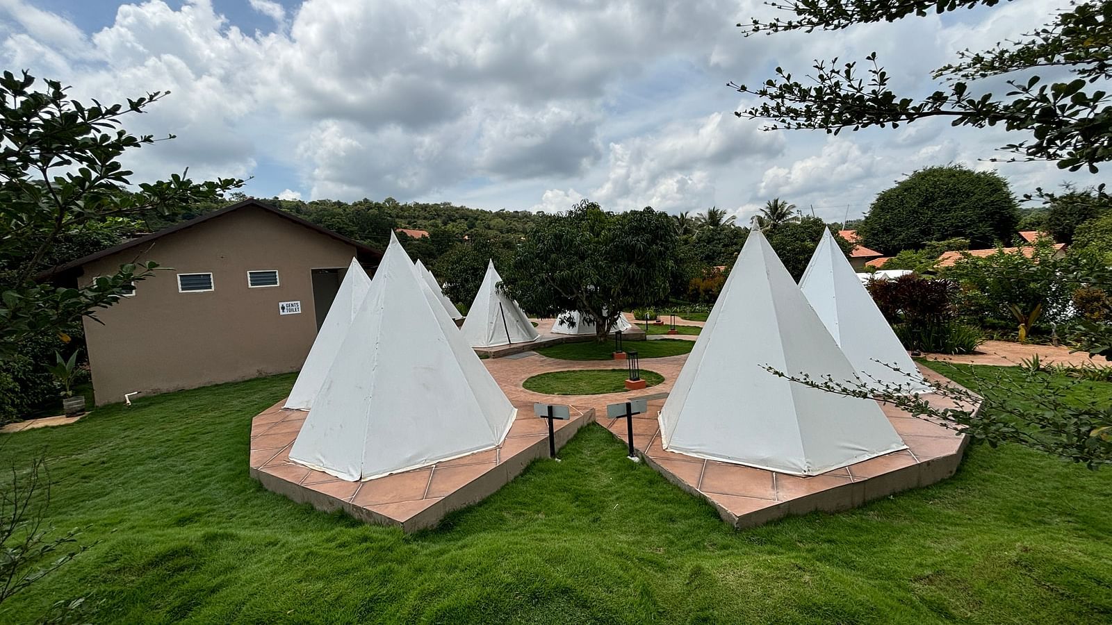 A scenic view of a resort area with tents lined along a neat walkway, surrounded by a well-maintained lawn.