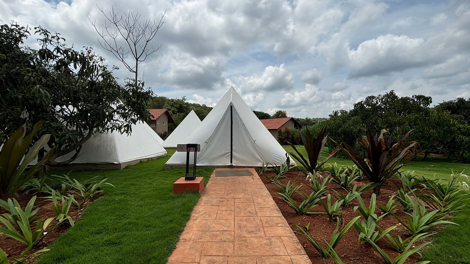 A scenic view of a resort area with tents lined along a neat walkway, surrounded by a well-maintained lawn.