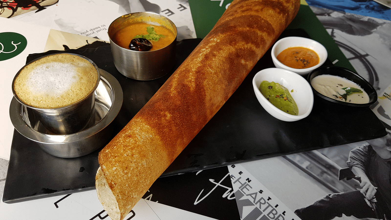 Masala dosa with chutney, sambhar and a side of coffee kept on a black plate