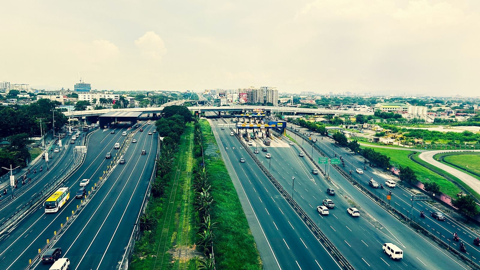 many lanes on a highway with vehicles moving on it and a toll booth in the background