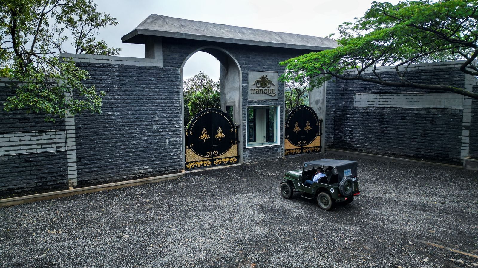 The front of a modern, grey stone building with a large gateway and a military jeep parked in the driveway - Tranquil Piedmont Estates & Resort, Lonavala
