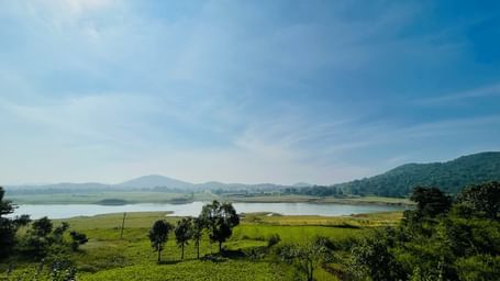 Scenic view of a lush green landscape with a river and hills under a bright blue sky.