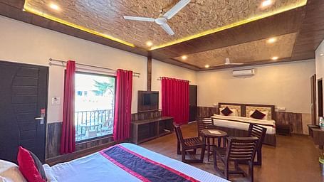 A Family Cottage with beds facing towards each other seperated by a round dining table and TV at DLS MJ River Resort, Rishikesh.