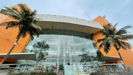 A modern glass-fronted building with palm trees framing the entrance under a clear sky