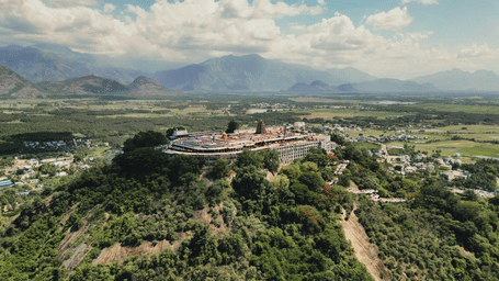 Aerial view of Arulmigu Sri Dhandayuthapani Swamy Thirukkovil perched atop a lush green hill with mountains in the background.