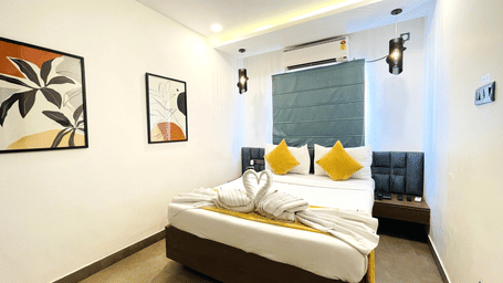King bed room at Hotel Kyzen Smart Stays Madhapur with yellow cushions, teal headboard panel, wall sconces, framed artwork, and wall-mounted air conditioner.