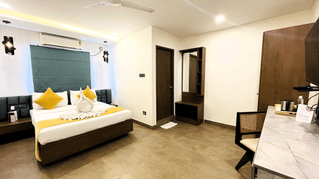 King bed room at Hotel Kyzen Smart Stays Madhapur featuring yellow cushions, teal headboard panel, wooden wardrobe, work desk, and room entrance door.