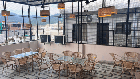 Full view of the rooftop restaurant at Perfectstayz Value Dhruv Nanda, Haridwar, with warm lights hanging from the tin ceiling along with a beautiful mountains in the background.
