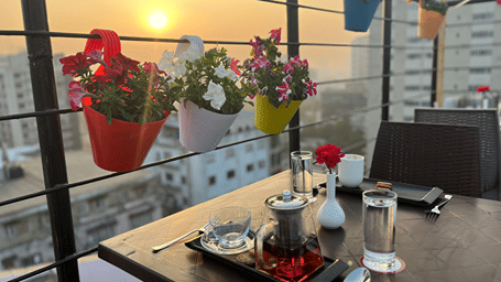 Rooftop dining setup with a table, beverages, snacks, small potted hanging plants, and a scenic view.