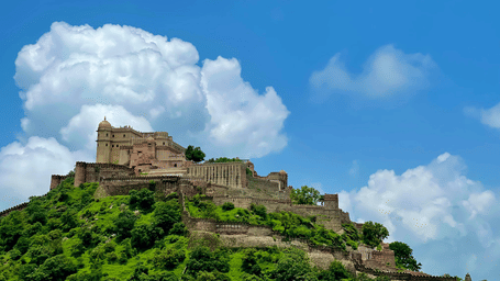 Kumbhalgarh Fort perched on a mountain surrounded by greenery under a blue sky with scattered clouds