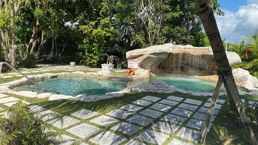 Outdoor pool area with stone flooring, surrounded by tropical greenery | A Stone's Throw Away
