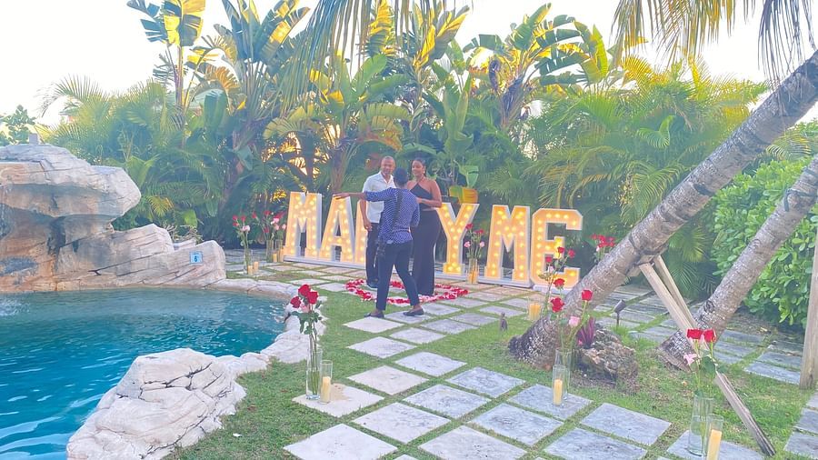Couple standing by poolside with illuminated MARRY ME sign in the background | A Stone's Throw Away