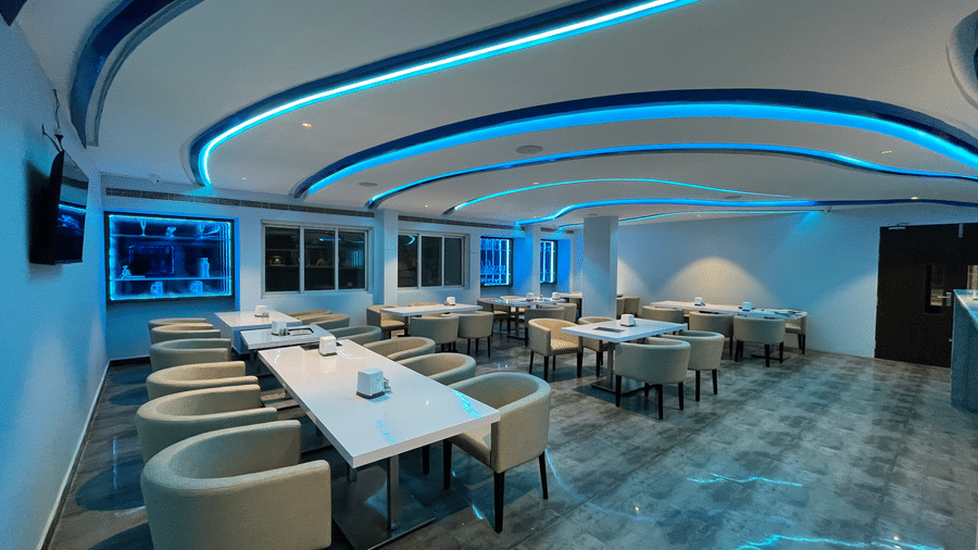 Modern bar interior with blue LED ceiling lights and stylish seating at Alps Residency, Krishnagiri.