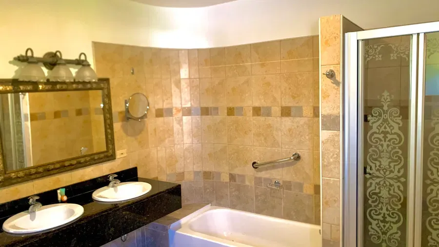 A tiled bathroom shows a bathtub, a vanity with two sinks, and a walk-in shower | Alexander Suite | Altamont Court, Jamaica
