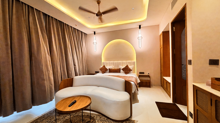 A bedroom features a curved white sofa, a round wooden coffee table, and a bed with an illuminated arched headboard at Avanya Resorts N Retreat.