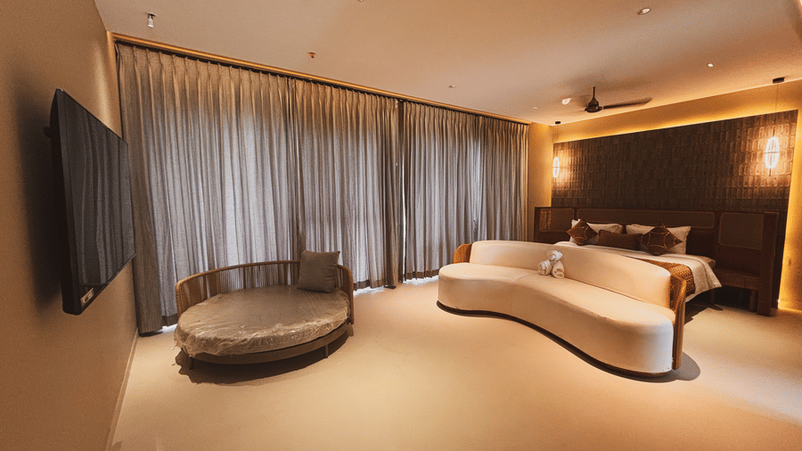 A large room contains a bed, a curved white sofa, a circular daybed, and a wall-mounted television at Avanya Resorts N Retreat.