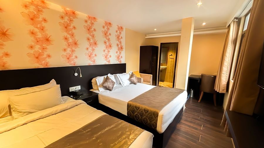 A bedroom with two queen size beds, a wardrobe, a table, and a chair at Avianna Hungry Jack, Gangtok.