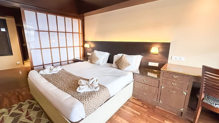 A bright bedroom with a neatly made bed, bedside tables, and wooden flooring at Avianna Hungry Jack, Gangtok.