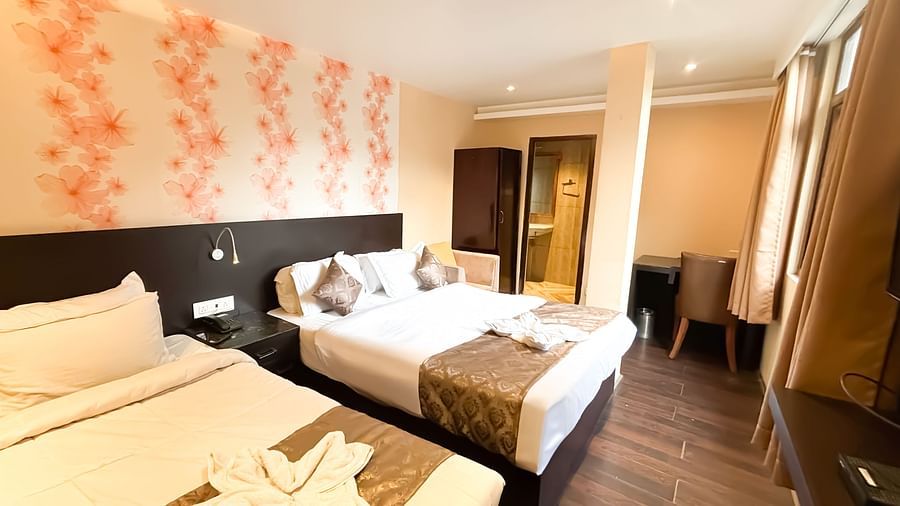 Side view of a twin bed room with flower-printed wallpaper behind the bed, at Avianna Hungry Jack, Gangtok.