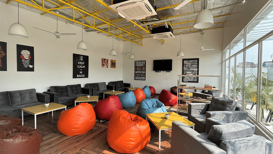 An image of a lounge area featuring sofas and bean bags for relaxation, coffee tables, and a bookshelf stocked with a selection of books to read.