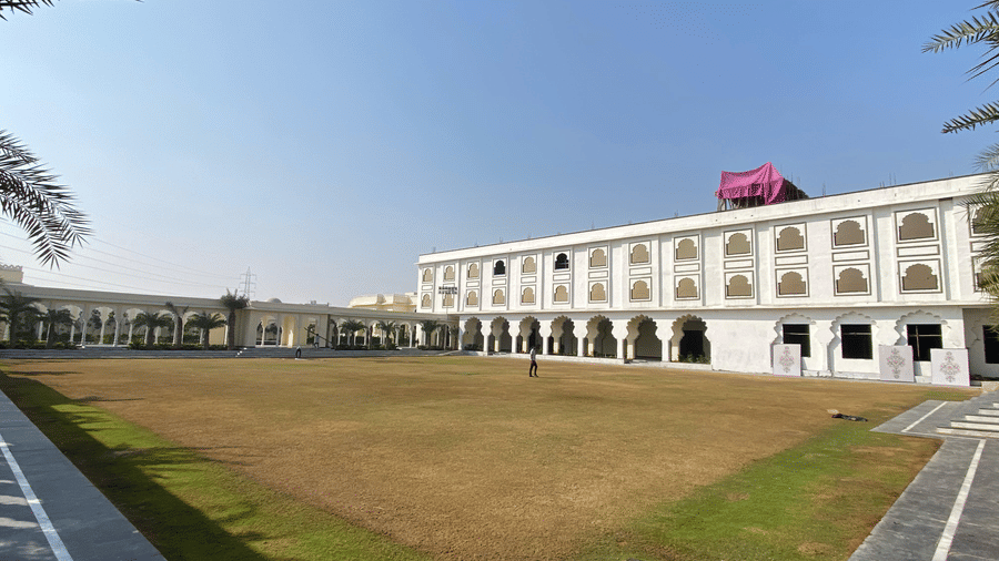 Large open lawn area bordered by multi-storey white building with arches at Beelwa Palace, Jaipur