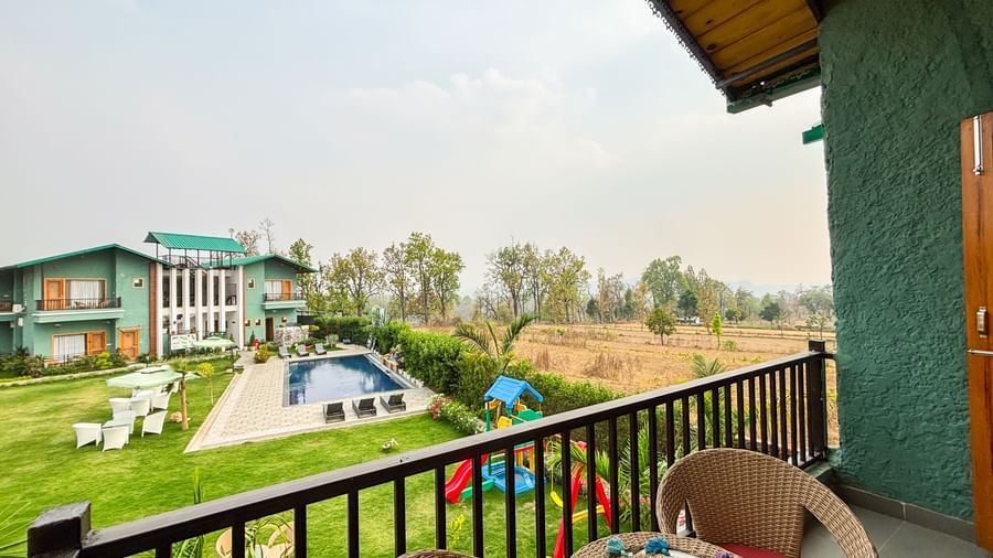 A serene balcony with chairs and a table overlooking a lush, green landscape, perfect for relaxing at Corbett Nirvana Resort.