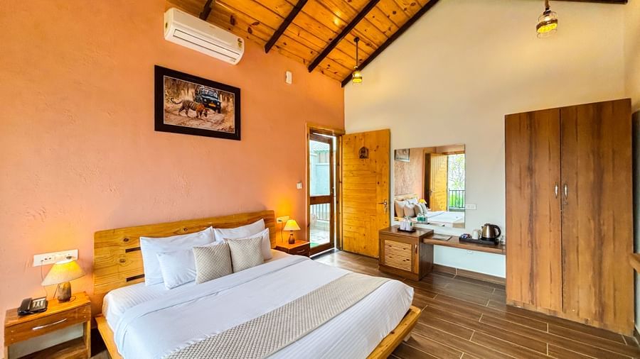 A cosy bedroom with a sloped wooden ceiling, a large bed, and warm-toned walls at Corbett Nirvana Resort..