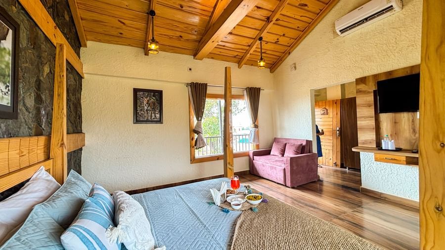 Spacious bedroom with wooden interiors and comfortable seating area at Corbett Nirvana Resort.