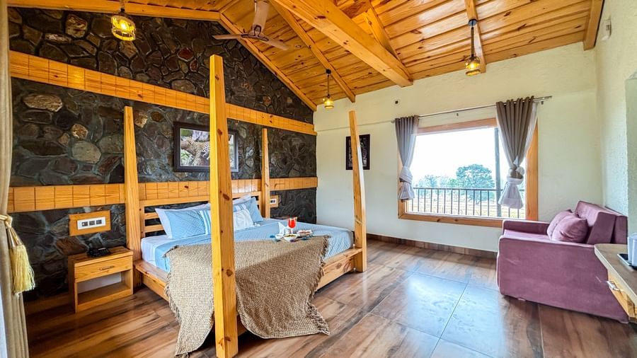 Bright bedroom with canopy bed, wooden ceiling, and balcony access at Corbett Nirvana Resort.