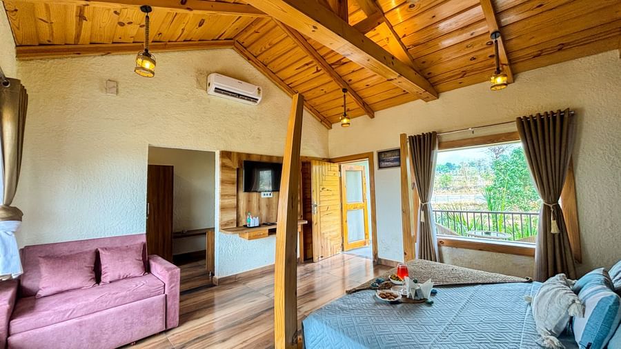 Spacious resort room with wooden ceiling, king-size bed, and sofa seating at Corbett Nirvana Resort.