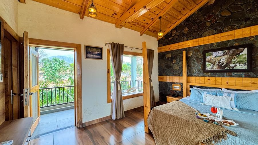 Spacious resort room with wooden ceiling, large windows, and balcony at Corbett Nirvana Resort.