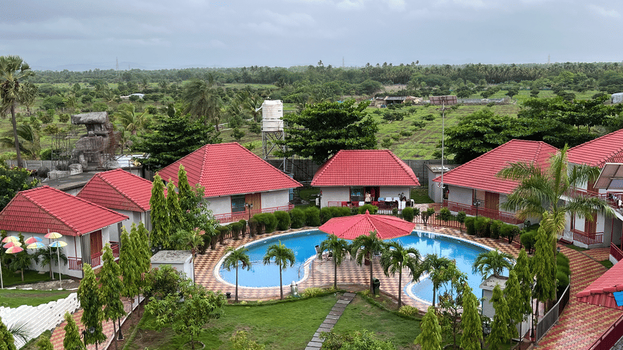 High-angle view of the circular swimming pool surrounded by red-roofed cottages - DAN Resorts & Weddings, Palghar