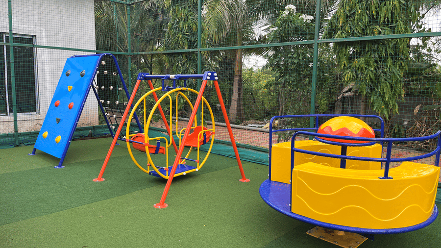 Children's outdoor play area featuring a climbing wall, merry-go-round, and swings on safety turf - DAN Resorts & Weddings, Palghar