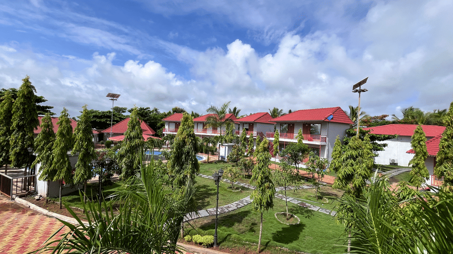 Scenic view of a row of red-roofed resort villas nestled among palm trees and manicured gardens - DAN Resorts & Weddings, Palghar