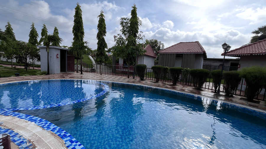Wide-angle view of the curved outdoor swimming pool under a bright sunny sky - DAN Resorts & Weddings, Palghar